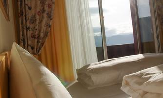 A cozy room with a bed and soft pillows. The sunlight streams through the window, creating a bright, inviting atmosphere.