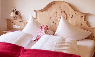 A cozy bedroom with a wooden headboard and white pillows. Red blankets give the room an inviting atmosphere.