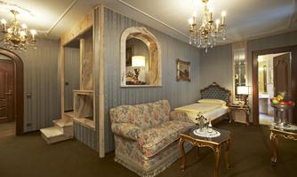 An elegant room with a cozy sofa and a comfortable bed. The walls are stylishly decorated, and several chandeliers create a warm atmosphere.