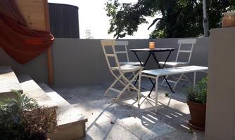 A small, cozy outdoor area with a table and two chairs. Some plants are placed in pots around the table.