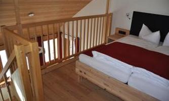 A cozy bedroom with wood paneling and modern furnishings. The bed has a red duvet, and there are large windows that let in a lot of light.