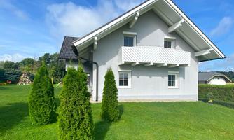 A modern house with a white balcony and green lawn area. In the foreground, there are some well-kept conifer-like plants.