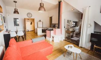 A modern apartment with a red sofa and an open kitchen area. The walls are light and there are wooden floors that create a warm atmosphere.