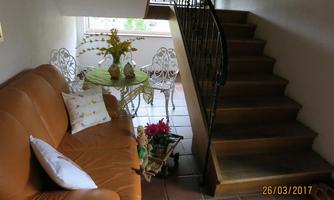 A cozy entrance area with a brown couch and a small table. A staircase leads upstairs, and there are some plants and decorations visible.