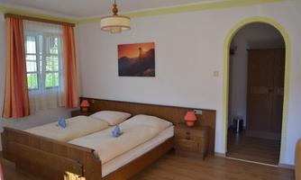 A cozy bedroom with two beds and wooden furniture. Soft colors and a window with curtains create an inviting atmosphere.