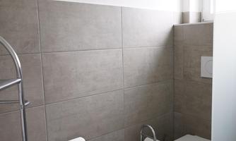 A modern bathroom with gray tiles and a toilet cubicle. There is a window and a metal towel holder.