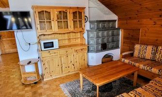 A cozy room with wooden paneling, a sofa, and a wooden table. In the background, a television and a stove are visible.