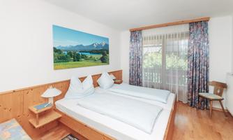 A cozy room with two single beds and wooden-paneled walls. The large window offers a view of nature and the mountains.