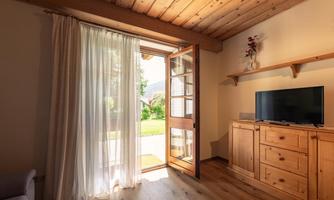 An inviting living space with an open door and a view of the garden. Bright and cheerful with natural wood and a television.