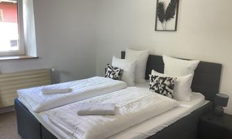 A modern bedroom with two single beds and bright pillows. A decorative picture with plant motifs hangs on the wall.