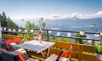 A cozy terrace with a table and chairs that offers a view of the mountains. On the table are glasses and a bottle, surrounded by beautiful nature.
