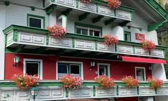 A beautiful house with balconies and colorful flowers. The facade is red and green, surrounded by a picturesque landscape.