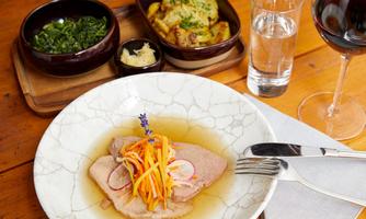A delicious dish with tender meat, colorful vegetables, and a flavorful broth. Side dishes and a glass of red wine are visible in the background.