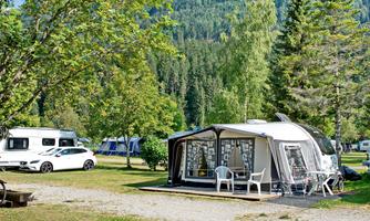 A camping scene with a caravan and a motorhome. Surrounded by green trees and grass, the site offers a relaxed atmosphere.