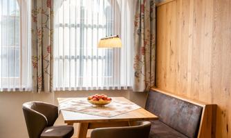 A cozy dining area with a wooden dining table and modern chairs. Large windows let in plenty of daylight.