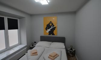 A modern bedroom with a gray bed and a large piece of art on the wall. There are fresh towels on the bed and a small bedside table.