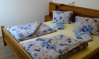 A cozy bedroom with a wooden bed and blue bedding. A painted picture hangs on the wall.
