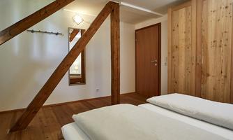 A cozy bedroom with a wooden ceiling and furniture. There are two beds available, and there is a mirror and a closed door.