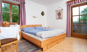 A cozy bedroom with a wooden bed and blue bedding. There is a table with fruit and large windows that lead to a balcony.