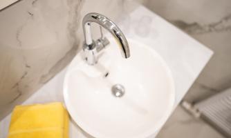 A modern sink with a shiny faucet. Next to it lies a yellow towel on a light surface.
