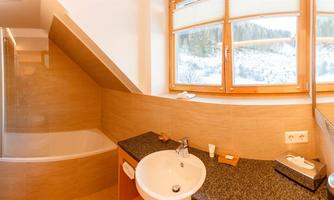 A modern bathroom with a bathtub and a sink. Large windows offer a view of the surrounding mountains.