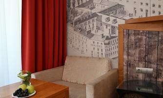 A cozy room with a beige armchair and a wooden table. On the table are fruits, and the wall is decorated with a drawing of buildings.