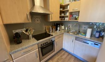 A modern kitchen with wooden cabinets and a gray countertop. Various kitchen appliances and utensils are visible.
