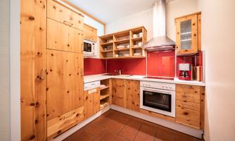 A modern kitchen with light wooden cabinets and red wall design. It is well-equipped with an oven and a microwave oven.