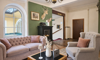 A stylishly furnished living room with a cozy sofa and an armchair. Pictures hang on the wall, and a deer head adorns the room.