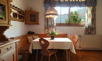 A cozy dining area with bright wood decor and a table in the middle. Large windows offer a view of the greenery and let in plenty of light.