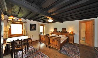 A cozy bedroom with two beds, a table and chairs. The room features wooden ceilings and a warm, inviting style.