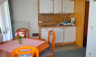 A cozy kitchen nook with a dining table and chairs. The amenities include a small stove, a sink, and a coffee machine.