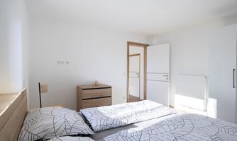 A bright bedroom with two beds and a modern wooden wardrobe. The walls are simple, and the room feels inviting and friendly.