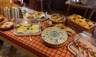 A rich buffet with various types of cheese, breads, and pastries. The tables are comfortably decorated and invite you to enjoy.