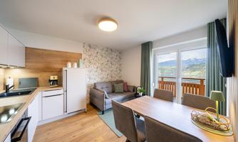 A modern kitchen with a cozy living room. The room has large windows with a view of the mountains.