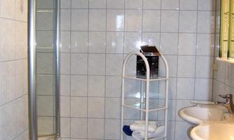 A modern bathroom with tiles and a shower. Towels and toiletries are placed on a shelf.