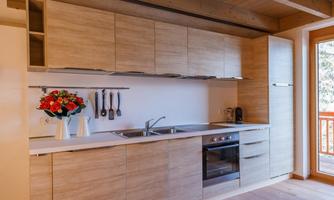 Modern kitchen with wooden cabinets and white surfaces. A bouquet of flowers and cooking utensils are visible.