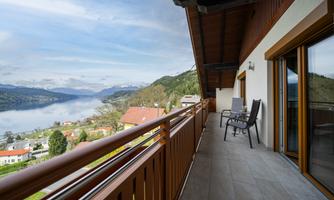 A beautiful balcony with a view of a picturesque lake and mountains. The surroundings are green and the atmosphere is calm.