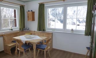A cozy dining area with a wooden table and wooden chairs. Large windows offer a view of the snow-capped mountains outside.