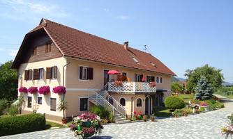 A beautiful house with a large garden and blooming plants. The terrace is equipped with a red sun umbrella.