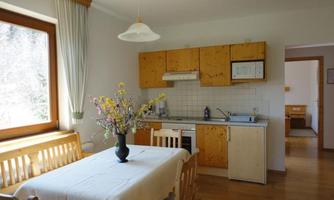 A cozy kitchenette with wooden cabinets and a dining table. A floral arrangement and the large window view create an inviting atmosphere.
