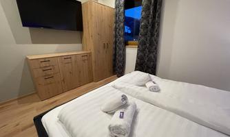 A cozy bedroom with a double bed and fresh towels. A television is hanging on the wall, and there is a wooden wardrobe as well as curtains.