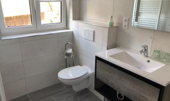 A modern bathroom with a bright tiled floor and white wall paneling. There is a basin with an undercounter and a window that lets in natural light.