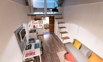 A modern, bright apartment with a cozy living area and stairs to the upper floor. The space is stylishly furnished with a dining area and a sofa.