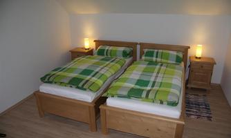 A cozy bedroom with two single beds covered with checkered blankets in green and white. Next to the beds are wooden nightstands with lamps.