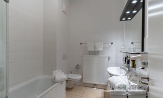 A modern bathroom with a bathtub and a shower. The walls are light and the fittings are clear and functional.