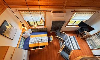 A cozy living and dining room with a wooden ceiling and modern furniture. The light from the lamps creates an inviting atmosphere.