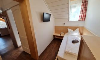 A simple room with a single bed and a television on the wall. The room has bright walls and a window with curtains in red.