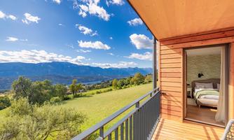 A balcony with a view of a green landscape and high mountains. The sky is clear with some clouds.