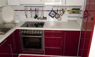 A modern kitchen with red furniture and a white countertop. The walls are decorated with kitchen utensils and spices.